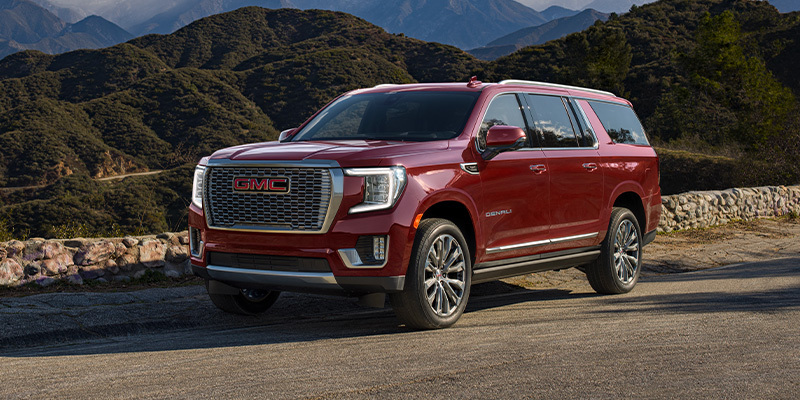 A red GMC Yukon XL parked in a scenic mountainous area.